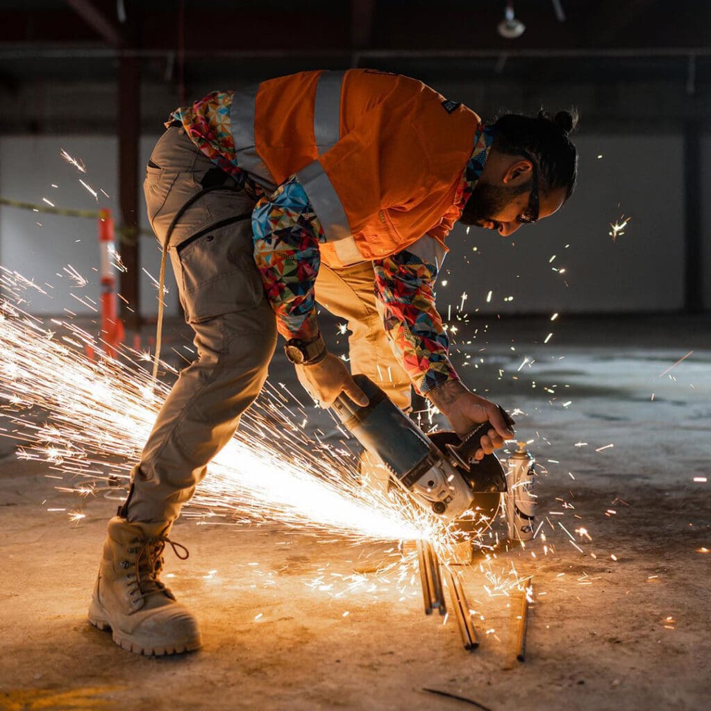 Project Demo demolition worker using an angle grinder to cut steel rods, with sparks flying around.