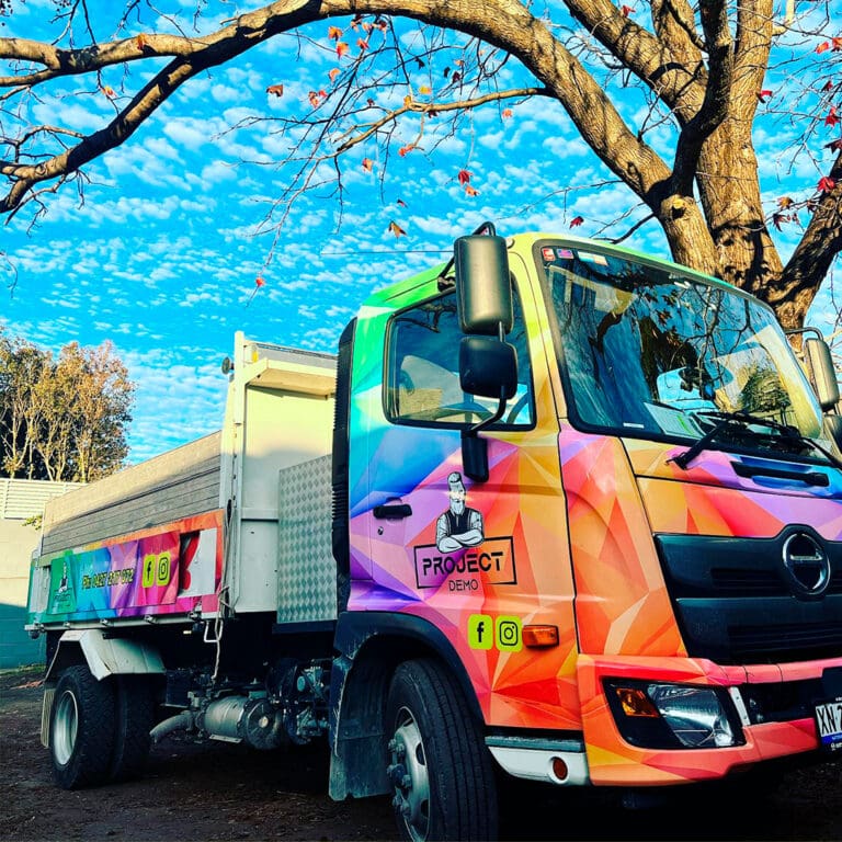 Colorful Project Demo truck parked under a tree with autumn leaves, showcasing company branding.
