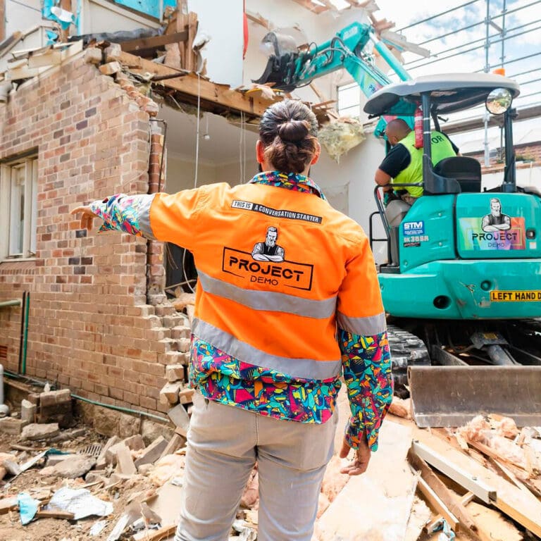 Demolition expert directing an excavator during a building teardown.