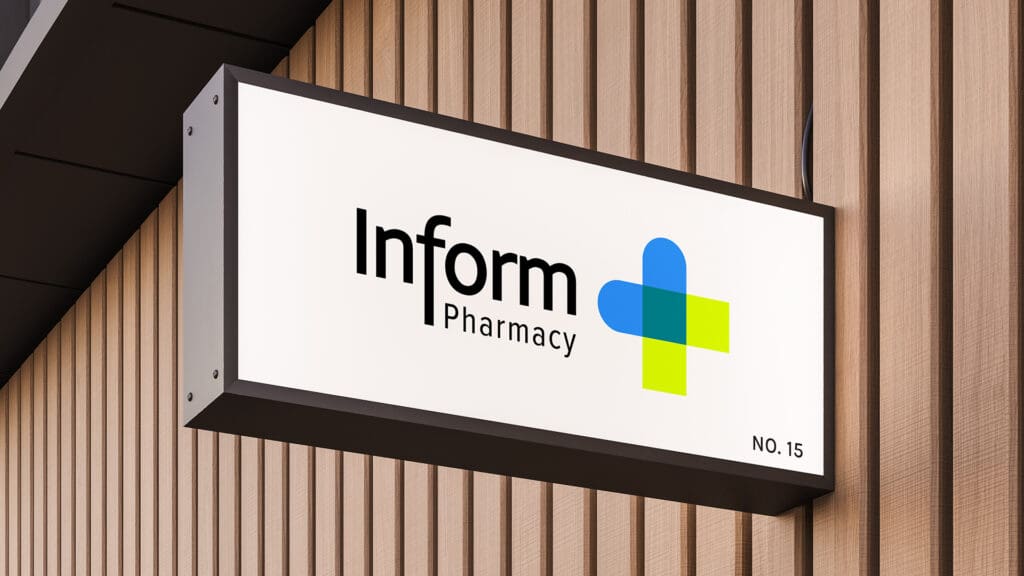 Outdoor rectangular signage for Inform Pharmacy featuring a modern logo with blue and green cross shapes, mounted on a wood-paneled wall